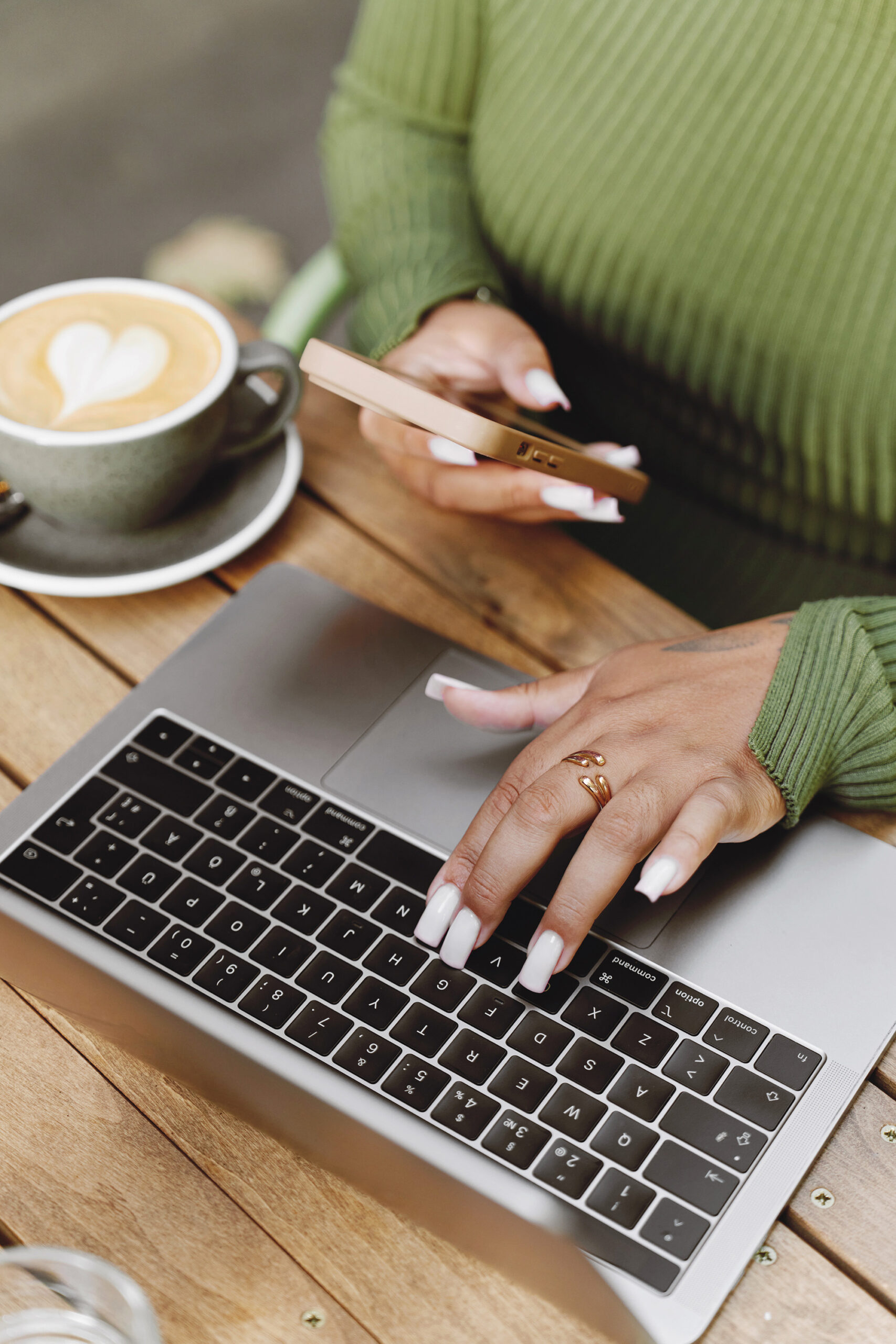 Woman using a laptop and phone at a coffee shop, representing connection and collaboration with The Rich Mommie.